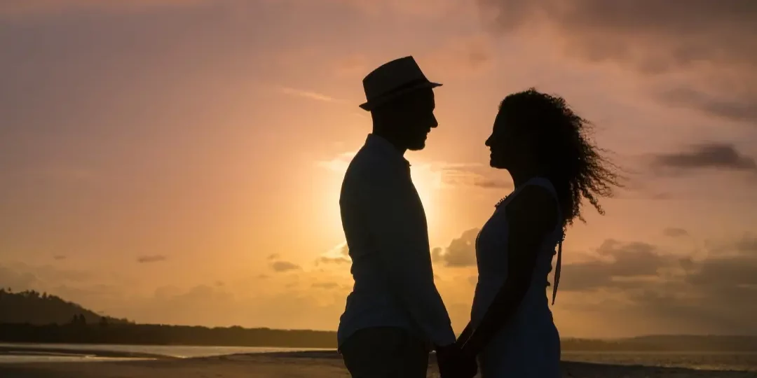 Ein Paar steht im Sonnenuntergang am Strand und zeigt so körperliche Nähe in der B Beziehung.