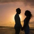 Ein Paar steht im Sonnenuntergang am Strand und zeigt so körperliche Nähe in der B Beziehung.