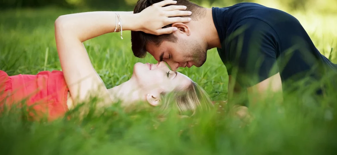 Ein Mann und eine Frau liegen im Gras und haben ihre Gesichter nah beieinander.