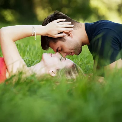Ein Mann und eine Frau liegen im Gras und haben ihre Gesichter nah beieinander.