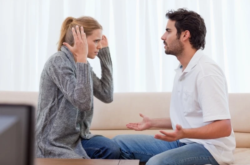 Fünf Phasen einer Beziehung: Ein Paar sitzt auf einem Sofa und streitet sich, was typisch ist für die Konfliktphase.