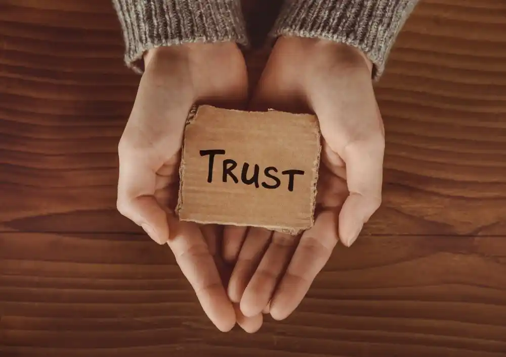 Zwei Hände halten ein Schild mit der Aufschrift Trust – Tipps, wie Paare Vertrauen nach einer Enttäuschung wieder aufbauen können